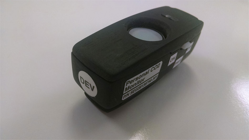 Shown is a colour photograph of a small black box with a sticker that reads “Personal CO2 Monitor.”