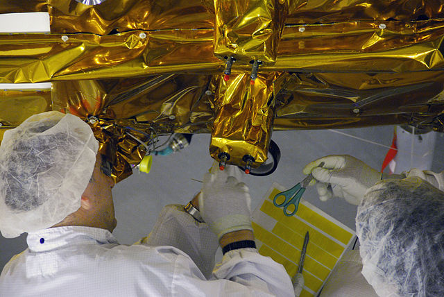 A colour photograph of two people working on a large object wrapped in shiny gold material.