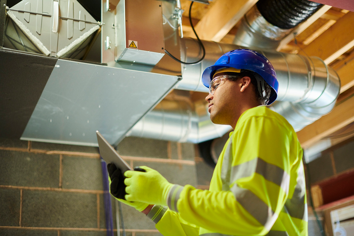 Shown is a colour photograph of a person in a hardhat studying a vent.