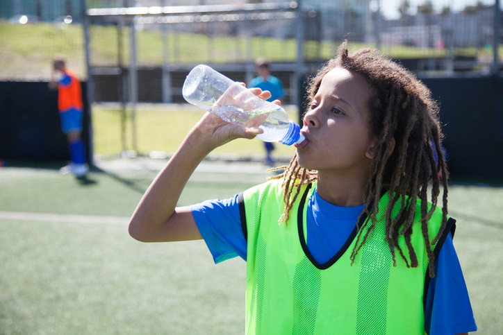Shown is a colour photograph of a student on a sports field, drinking from a bottle of water.