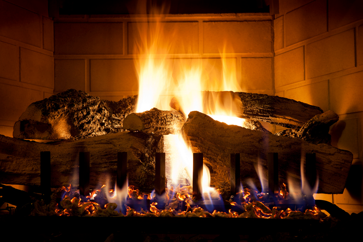 Shown is a colour photograph of orange flames around dark logs inside a fireplace.